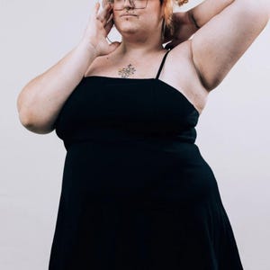 May include: A solid black mini dress featuring a straight neckline and thin spaghetti straps. The garment has a fitted bodice that transitions into a slightly flared skirt, providing a simple and clean silhouette without any additional patterns or textures.