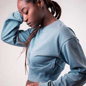 May include: A person wearing a blue cropped sweatshirt with long sleeves.