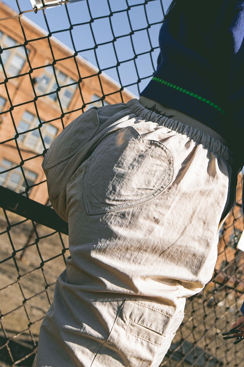 K&ouml;nnte beinhalten: Beige Cargohose mit einem herzf&ouml;rmigen Patch auf der Ges&auml;&szlig;tasche.