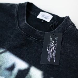 May include: Black t-shirt with a white graphic print of a hand reaching towards another hand. The t-shirt has a tag attached that says "Artcare Shop" and "AD-Careshop".