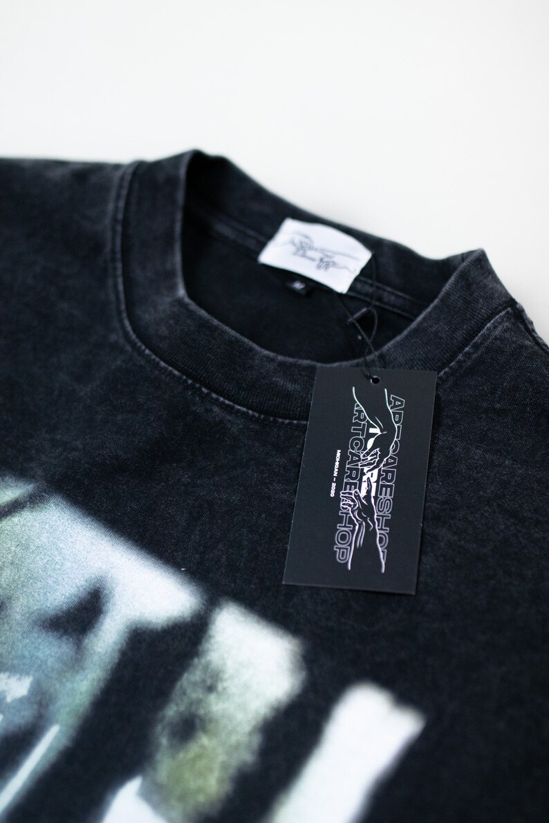 May include: Black t-shirt with a white graphic print of a hand reaching towards another hand. The t-shirt has a tag attached that says "Artcare Shop" and "AD-Careshop".