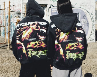 May include: Two black hoodies featuring a graphic print of a face with fangs and the word "Imagine" on the back. The hoodies have a drawstring hood and a kangaroo pocket.