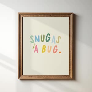 May include: A framed print with the text "Snug as a bug." in colorful letters. A small green insect is climbing the letter "A".