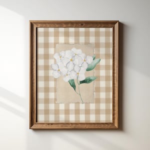 Op de afbeelding: Een ingelijst afdruk van een aquarel van witte bloemen op een bruin-witte ruitjesachtergrond.