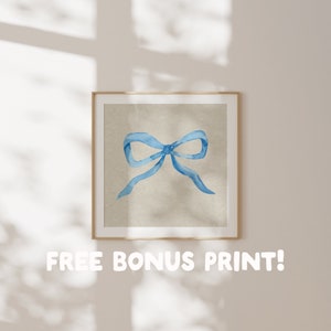 May include: A framed print of a watercolor painting of a blue bow on a beige background.