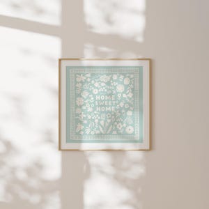 May include: A framed print with a light blue background and white floral design. The text "Home Sweet Home" is centered in the design.