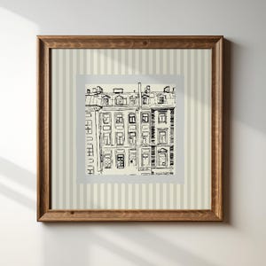 Può includere: Una stampa incorniciata con uno schizzo architettonico in bianco e nero di una facciata di un edificio. L'opera d'arte è ambientata su uno sfondo color crema con strisce verticali e racchiusa in una cornice di legno marrone. La stampa mostra finestre, porte e tetti.