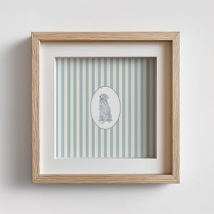 May include: A framed print featuring a seated dog illustration within an oval frame. The background has vertical stripes in light blue and off-white. The frame is made of light-colored wood.