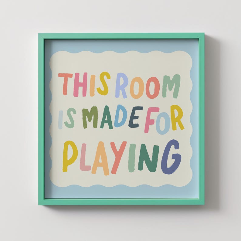 May include: A framed print with a light blue background and a white wavy border. The text "THIS ROOM IS MADE FOR PLAYING" is written in colorful, playful letters.