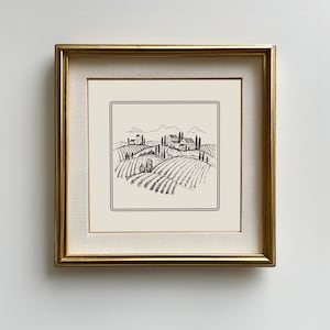 以下が含まれることがあります： なだらかな丘、農家、木々のある田園風景の白黒線画。絵は金色の額縁に入っています。
