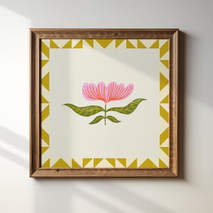May include: A framed print of a stylised pink flower with green leaves on a cream background. The frame is brown wood with a gold geometric border.