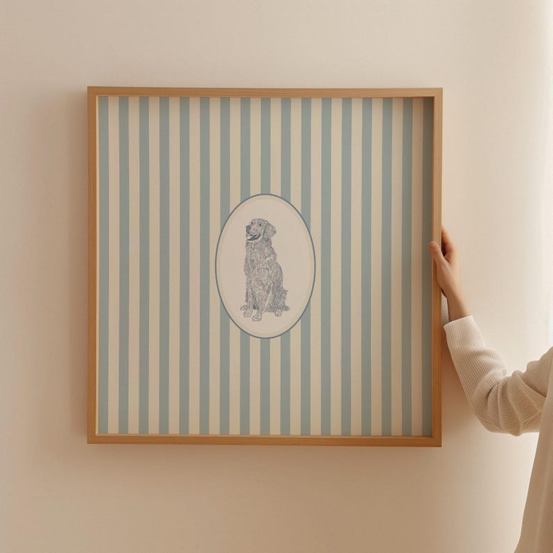May include: A framed artwork featuring a seated dog illustration within an oval, set against a backdrop of vertical blue and cream stripes. The frame is made of light-colored wood, and the overall aesthetic is classic and decorative.