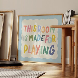 May include: A framed print with a light blue background and white border. The text "This room is made for playing" is written in colorful, playful letters.
