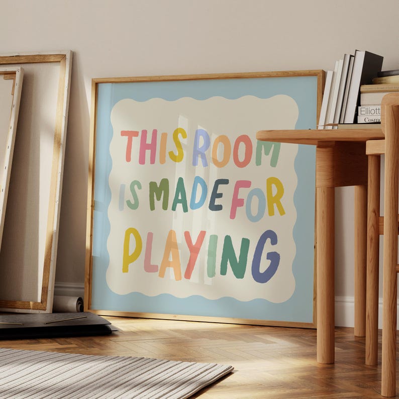 May include: A framed print with a light blue background and white border. The text "This room is made for playing" is written in colorful, playful letters.