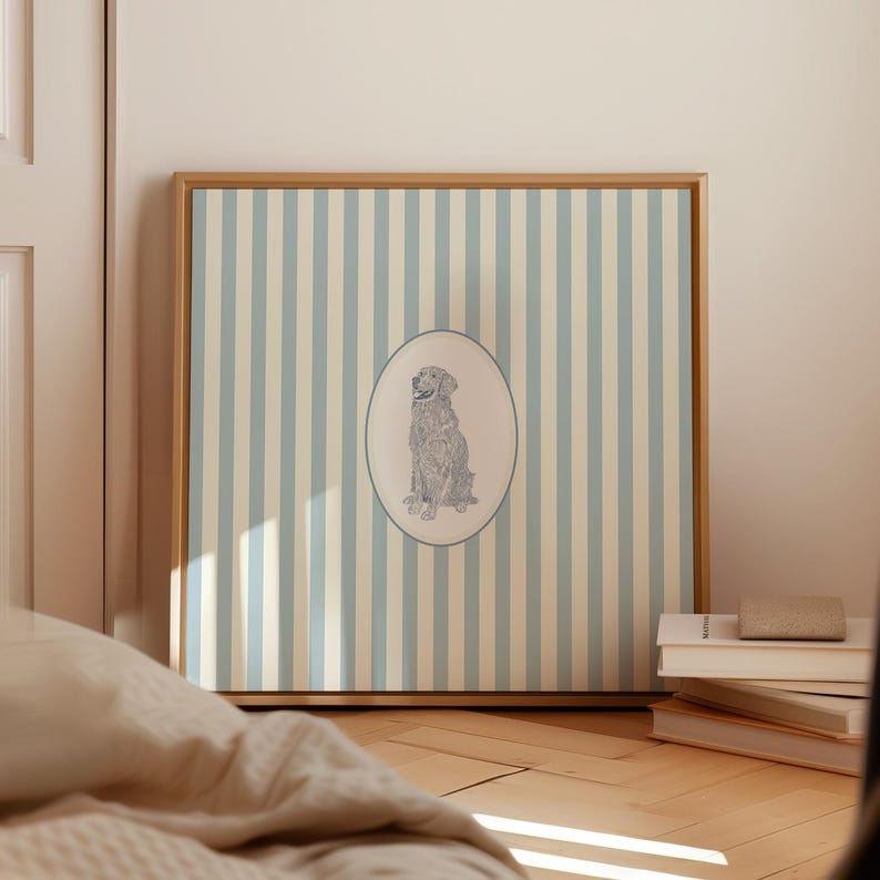 May include: A framed print featuring a dog illustration within an oval on a striped background. The artwork has a light blue and beige color scheme, with a natural wood frame. The print is displayed on a wooden floor.