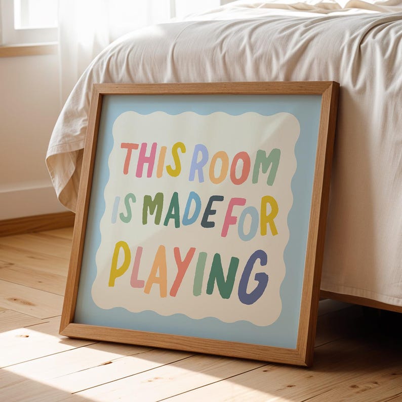 May include: A framed print with a light blue background and a white border. The text "THIS ROOM IS MADE FOR PLAYING" is written in colorful, playful letters.