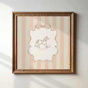 May include: A framed print with a rocking horse illustration. The artwork has a background of vertical cream and peach stripes. The frame is made of dark wood, adding a classic touch to the nursery decor.