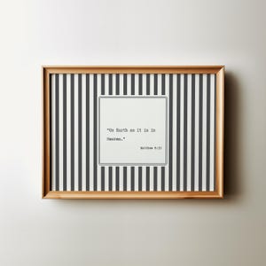 May include: A framed print with a light wood frame. The print has a black and white striped background with a white square in the centre containing the quote "On Earth as it is in Heaven." and the reference Matthew 6:10.