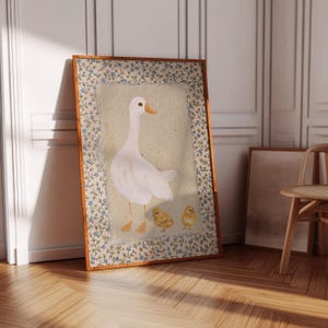 Peut inclure: Une illustration encadr&eacute;e d'une oie blanche avec deux oisons jaunes. L'oie est debout, les ailes baiss&eacute;es, la t&ecirc;te tourn&eacute;e sur le c&ocirc;t&eacute;. Les oisons sont debout derri&egrave;re l'oie, la regardant. L'illustration est entour&eacute;e d'une bordure florale.