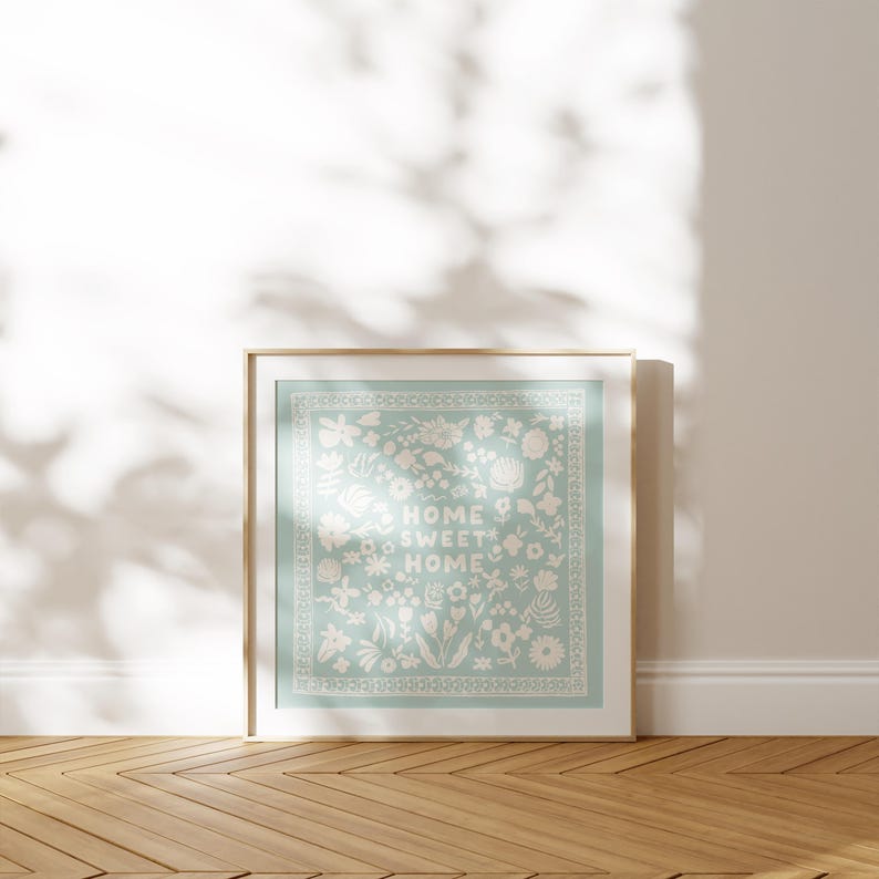 May include: A framed print with a light blue background and white floral design. The text "Home Sweet Home" is centered in the design.