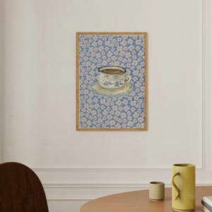 May include: A framed print of a blue and white teacup with a saucer on a blue background with white flowers.