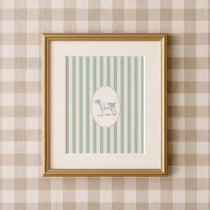 May include: A framed print featuring a dog illustration within an oval, set against a backdrop of vertical blue and cream stripes. The print is encased in a gold frame, adding a touch of elegance to the artwork.