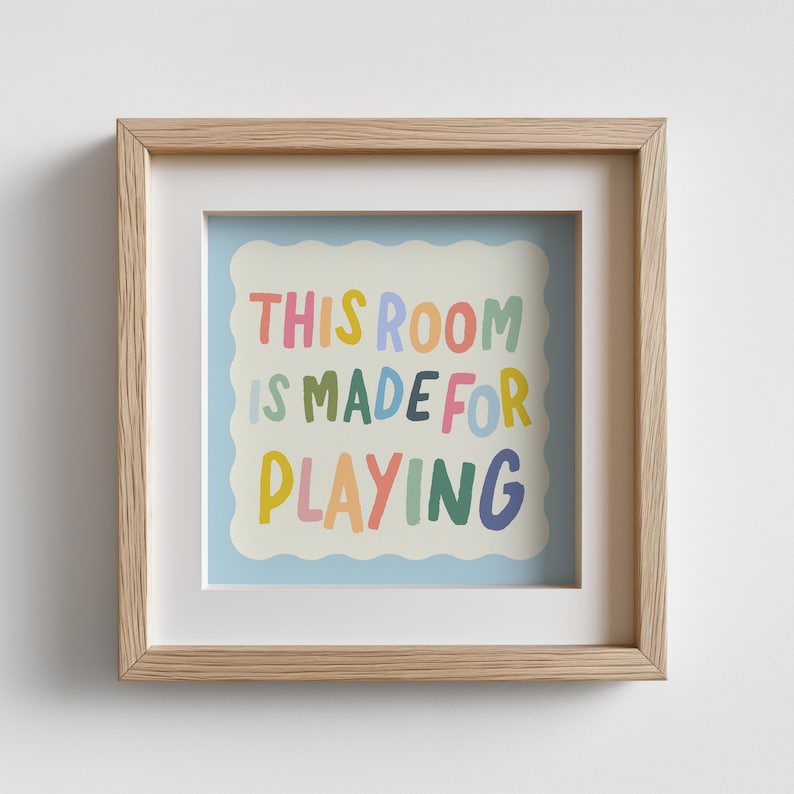 May include: A framed print with a light blue background and a white scalloped border. The text "THIS ROOM IS MADE FOR PLAYING" is written in colorful, playful letters.