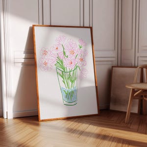 May include: A framed art print featuring a sketch of pink flowers in a glass vase with blue water. The artwork has a brown wooden frame and is leaning against a white wall. The floor is made of wood.