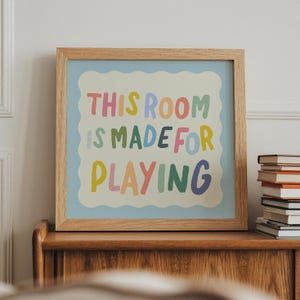 May include: A framed print with a light blue background and a white border. The text "This room is made for playing" is written in colorful letters.