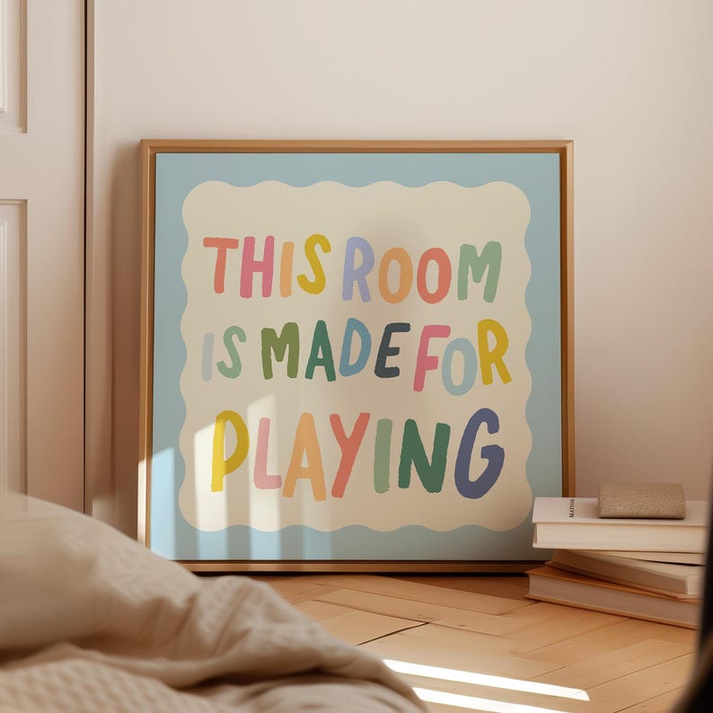 May include: A framed print with a light blue background and a white cloud-shaped border. The text "This room is made for playing" is written in colorful, playful letters.