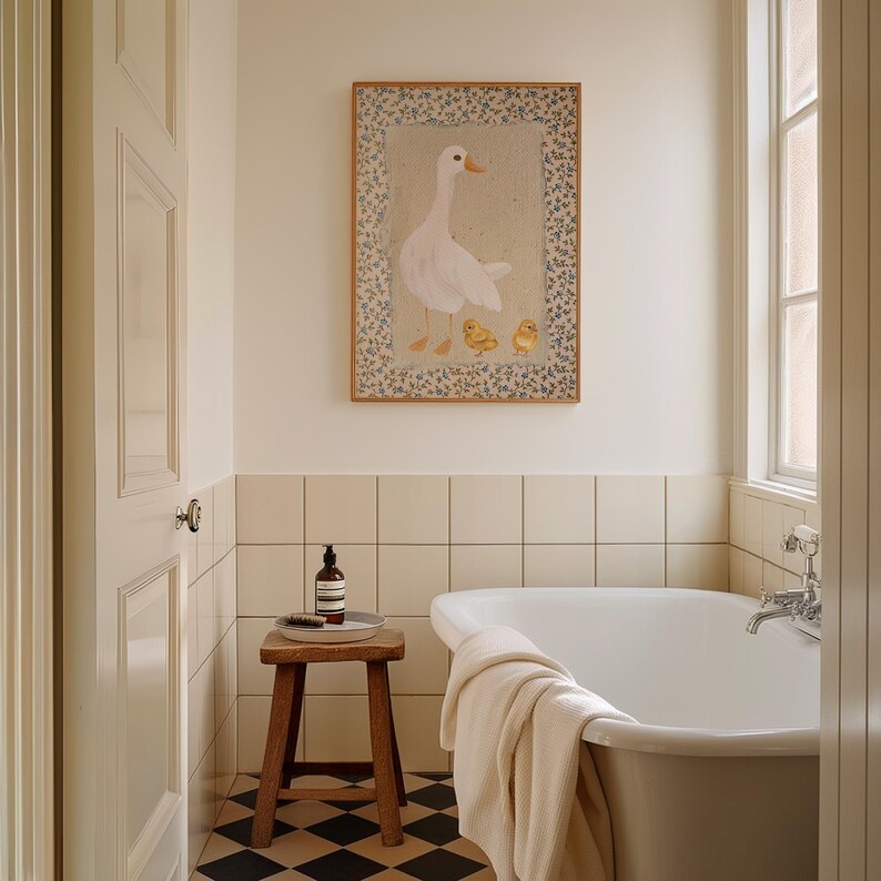 Peut inclure: Une oie blanche avec trois poussins jaunes dans une illustration encadr&eacute;e au-dessus d'une baignoire blanche dans une salle de bain avec des carreaux beiges et un sol en damier noir et blanc.