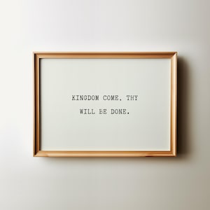 Può includere: Una stampa incorniciata con il testo "KINGDOM COME, THY WILL BE DONE." Il testo è in un semplice carattere, centrato su uno sfondo bianco. La cornice è in legno di colore chiaro.