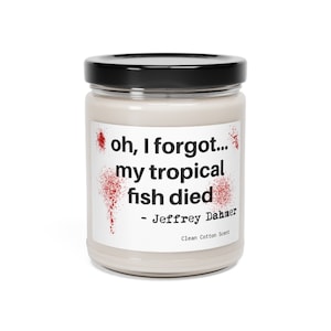 Puede incluir: Un tarro de vela blanco con tapa negra. El tarro tiene un patrón de salpicaduras rojas y texto negro que dice "oh, se me olvidó... mi pez tropical murió - Jeffrey Dahmer Aroma de algodón limpio".