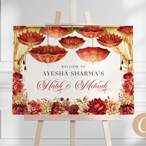 May include: Welcome to Ayesha Sharma's Haldi & Mehndi sign with a red and gold floral design and hanging umbrellas.