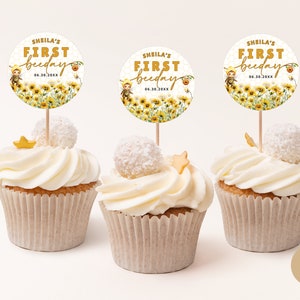 May include: Three yellow and white cupcakes with white frosting and a gold star on top. Each cupcake has a round, white and yellow paper topper with the text "Sheila's First Beeday 06.30.20XX" in gold lettering.