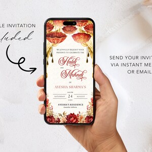 K&ouml;nnte beinhalten: Der Bildschirm eines Mobiltelefons zeigt eine digitale Einladung zu einer Haldi- und Mehndi-Zeremonie f&uuml;r Ayesha Sharma. Die Einladung zeigt ein florales Design mit roten und goldenen Akzenten. Der Text lautet: "Wir bitten Sie herzlich, an der Feier des Haldi und Mehndi von Ayesha Sharma am Samstag, den 24. August 20XX, in Ayeshas Residenz in Greenville, Kalifornien, teilzunehmen."