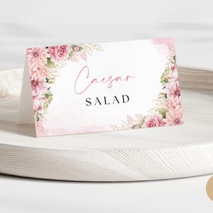 Pode incluir: Um cartão de mesa de casamento com design floral rosa e o texto "Caesar Salad" impresso em preto.