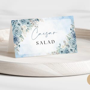Pode incluir: Cartão de mesa de casamento floral azul e branco com o texto "Salada Caesar".