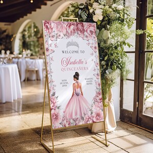 May include: A pink and white welcome sign with butterflies and floral accents. The sign reads "Welcome to Isabella's Quincea&ntilde;era" with the date "30th of June, 20XX" and the location "Majestic Haven Hotel".