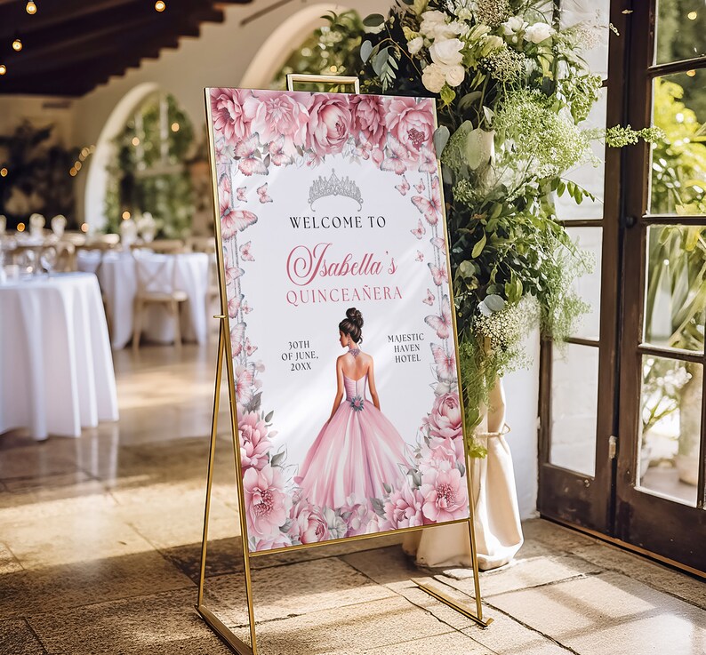 May include: A pink and white welcome sign with butterflies and floral accents. The sign reads "Welcome to Isabella's Quincea&ntilde;era" with the date "30th of June, 20XX" and the location "Majestic Haven Hotel".
