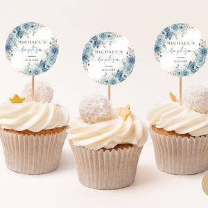 Pode incluir: Três cupcakes com cobertura branca e toppers florais azuis e brancos que dizem "Batismo do Michael" com uma data.