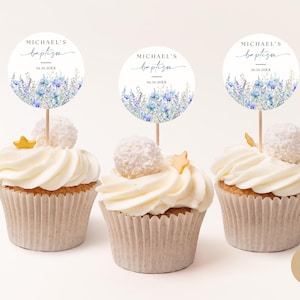 Pode incluir: Três cupcakes brancos com cobertura branca e toppers de estrela dourada. Cada cupcake tem um topper redondo de papel branco com flores azuis em aquarela e o texto "MICHAEL'S baptism" em preto.