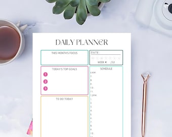May include: A daily planner with a pink, yellow, and teal color scheme. The planner has sections for "This Month's Focus", "Today's Top Goals", "To Do Today", and "Schedule". There are also sections for "Drink Up" and "B", "L", and "D".