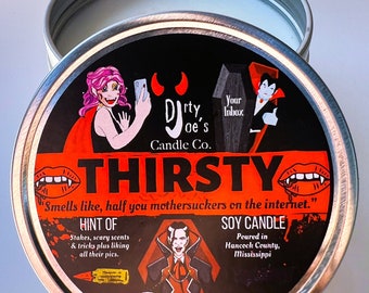 May include: A black and silver candle tin with a red and black illustration of a vampire. The text on the tin reads "Dirty Joe's Candle Co. Thirsty "Smells like, half you mothersuckers on the internet." Hint of: Stakes, scary scents & tricks plus liking all their pics. Soy Candle Poured in Hancock County, Mississippi"
