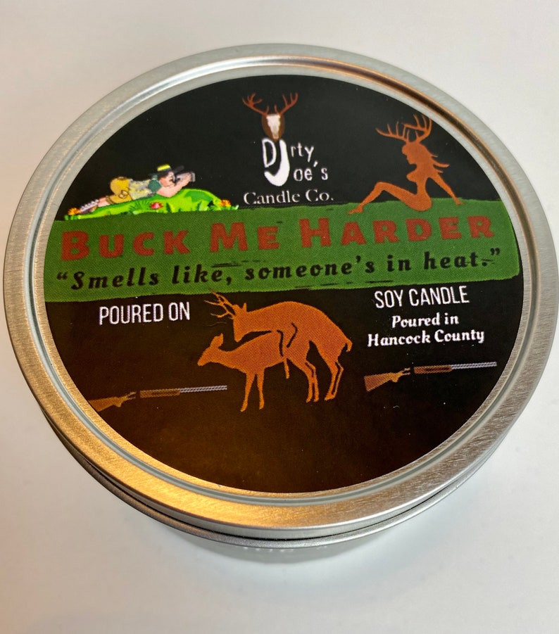 May include: A round, silver-colored candle tin with a black label. The label features the text "BUCK ME HARDER" and "Smells like, someone's in heat." along with deer illustrations and the words "SOY CANDLE". The candle is from Dirty Joe's Candle Co.