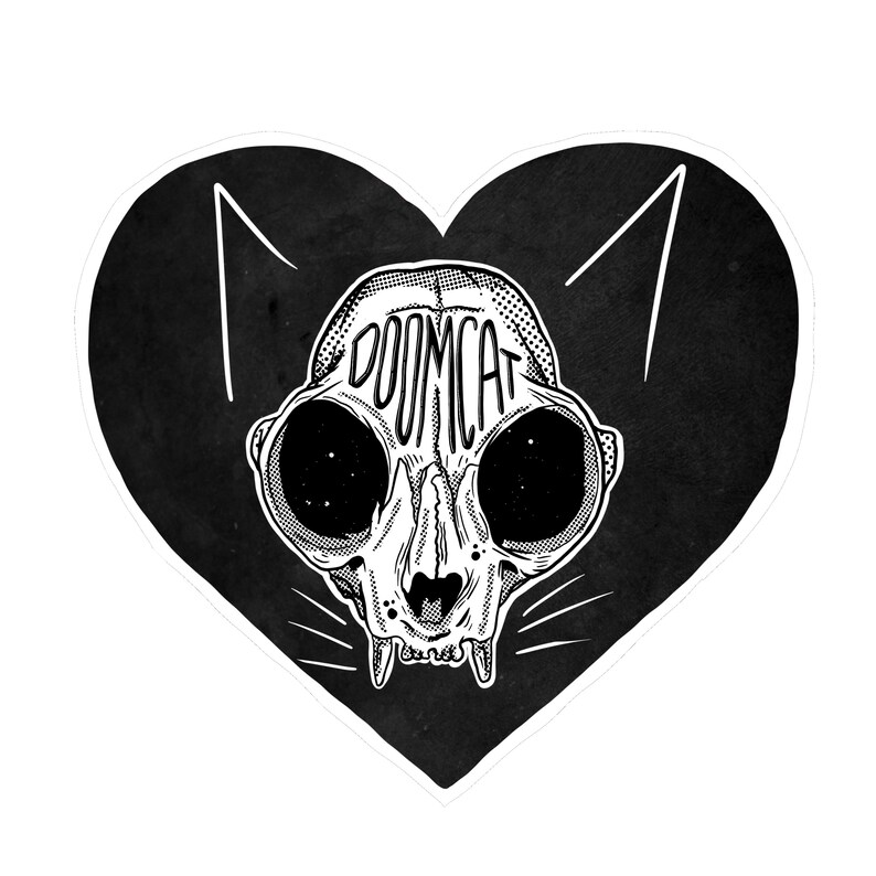 May include: Black and white illustration of a cat skull with the word "DOOMCAT" written across the forehead, inside a heart shape.