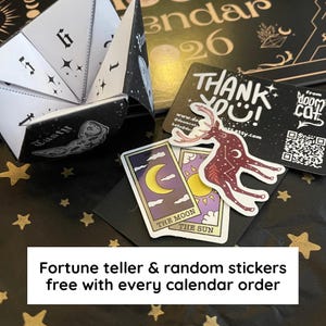 May include: A black and white fortune teller with numbers and stars, next to tarot cards and stickers. The cards feature a crescent moon and sun. The text reads "Fortune teller & random stickers free with every calendar order."
