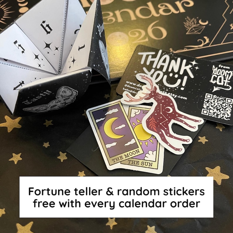 May include: A black and white fortune teller with numbers and stars, next to tarot cards and stickers. The cards feature a crescent moon and sun. The text reads "Fortune teller & random stickers free with every calendar order."