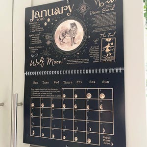 May include: Black and gold wall calendar for January 2020, featuring a wolf illustration and moon phase details. Includes text: "Wolf Moon", "Vision Board", and "The Fool". The calendar has a spiral binding and is hanging on a white door.