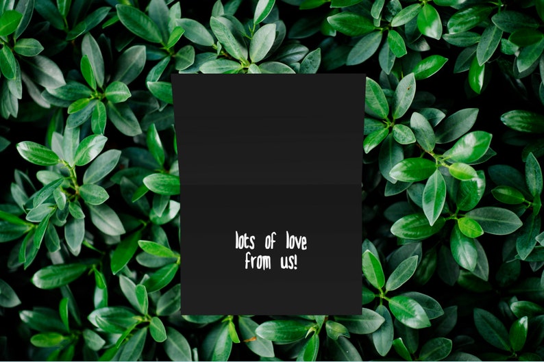May include: A black card with the text "lots of love from us!" written in white on it. The card is surrounded by green leaves.